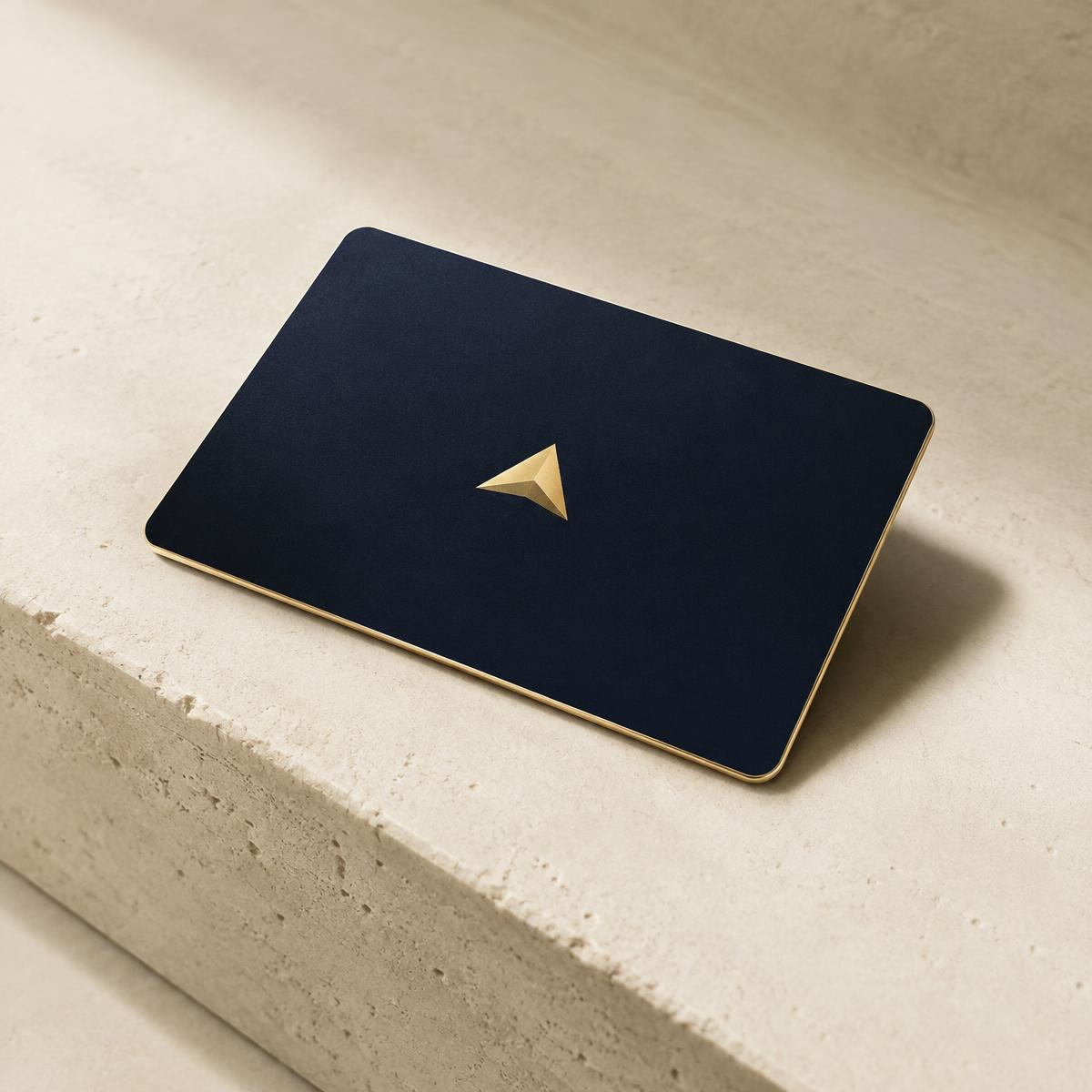 A navy card with a gold edge and triangle emblem on ivory stone